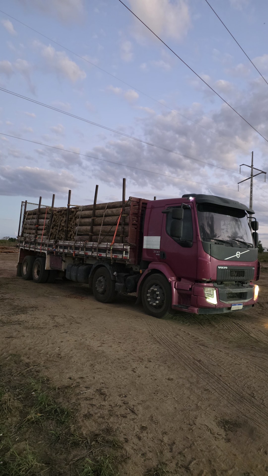 Caminhão vinho com carga de madeira ao entardecer